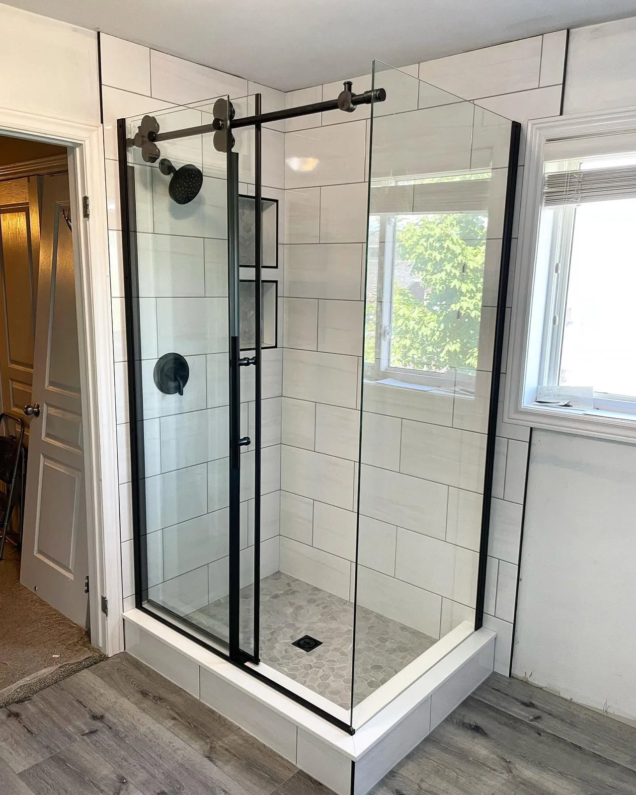 The finished shower in the corner, black framed sliding glass beside the window