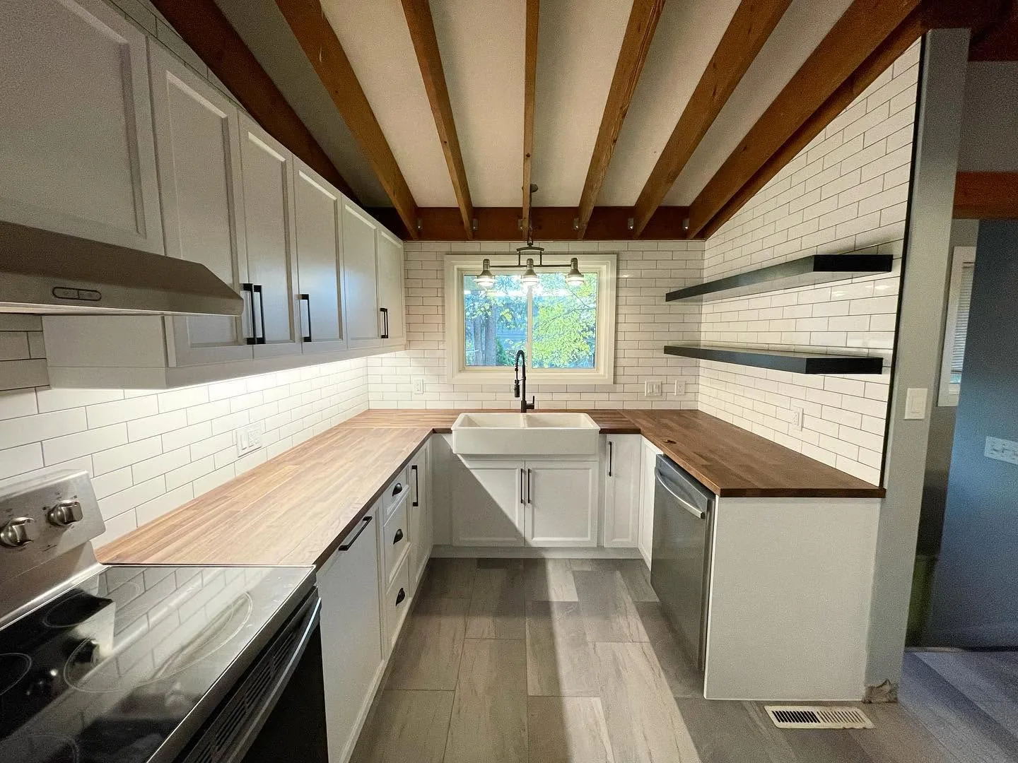 The finished kitchen under the exposed beams, butcher block and floating shelves