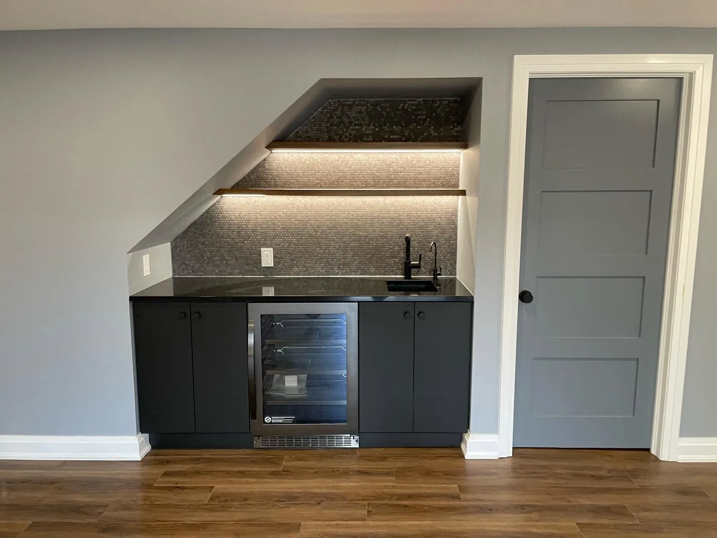 The bar built into the slope under the staircase, penny round tile lit from under the shelves