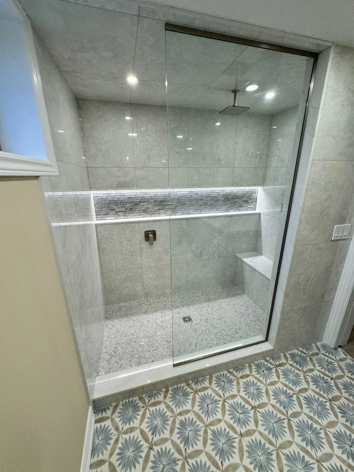 Grey marble shower with a mosaic accent band, corner bench and frameless glass