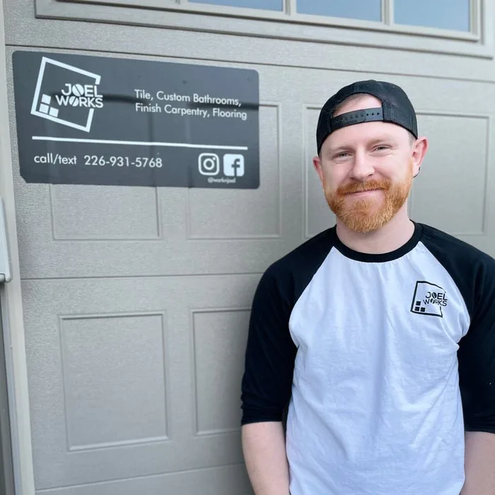 Joel outside a garage, beside his Joel Works sign