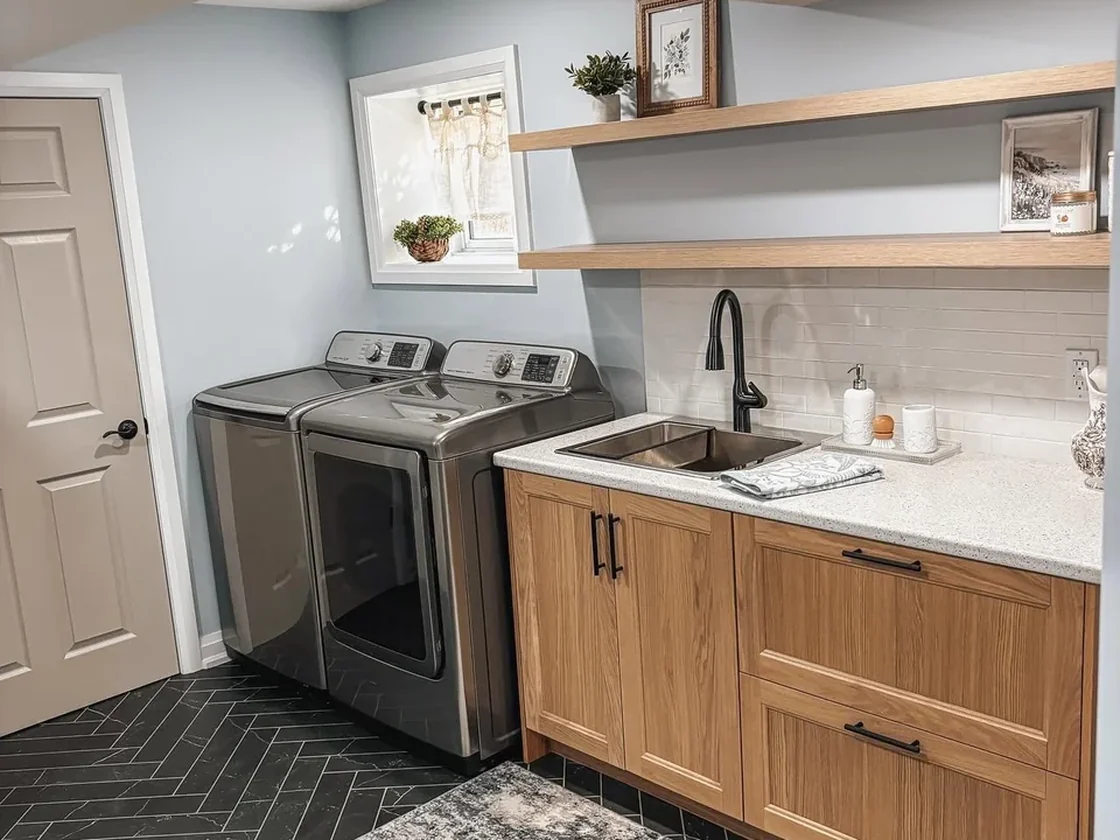 Finished basement laundry with oak cabinetry and herringbone tile