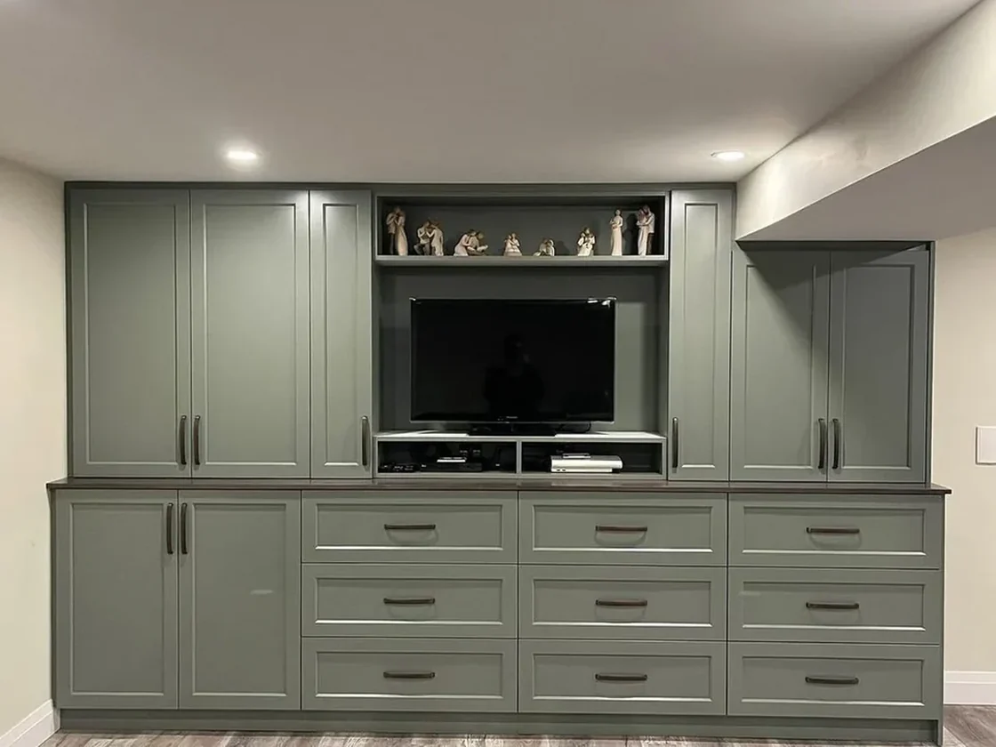 Built-in media wall in sage green with drawer banks and lit shelving