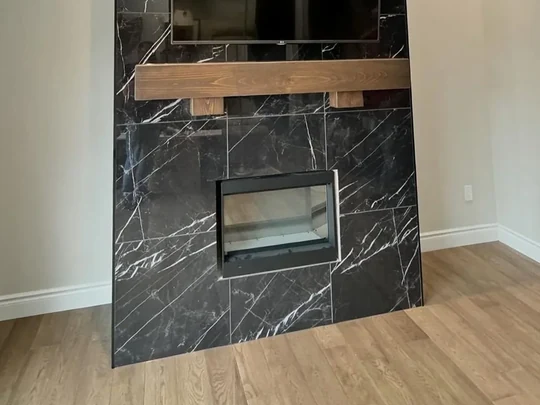 Black marble-look surround around a see-through firebox, with a solid timber mantel