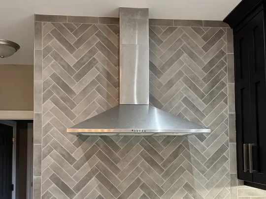 Herringbone tiled range wall behind a stainless chimney hood