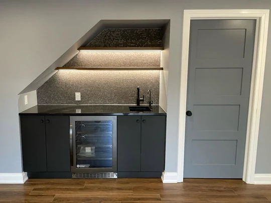 Basement wet bar with lit shelving and a beverage fridge